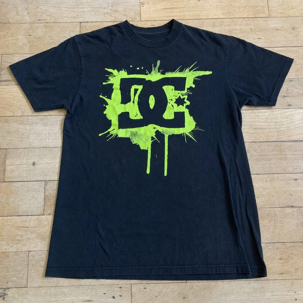 Camiseta preta DC GREEN SPLASH esticada, estampa completa