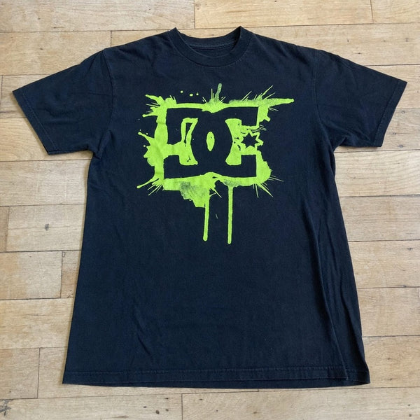 Camiseta preta DC GREEN SPLASH esticada, estampa completa